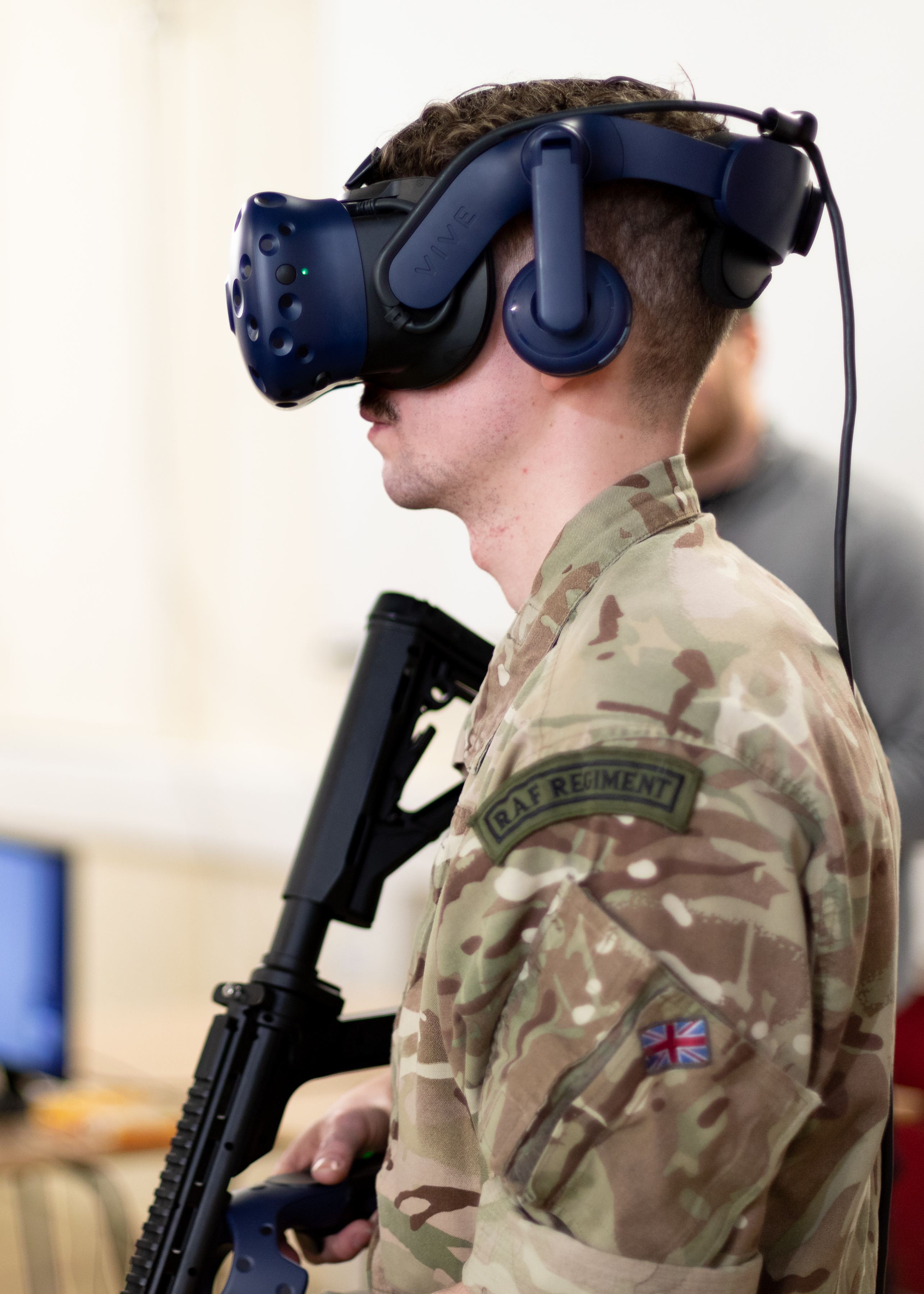 Personnel holds rifle while wearing virtual reality headset.